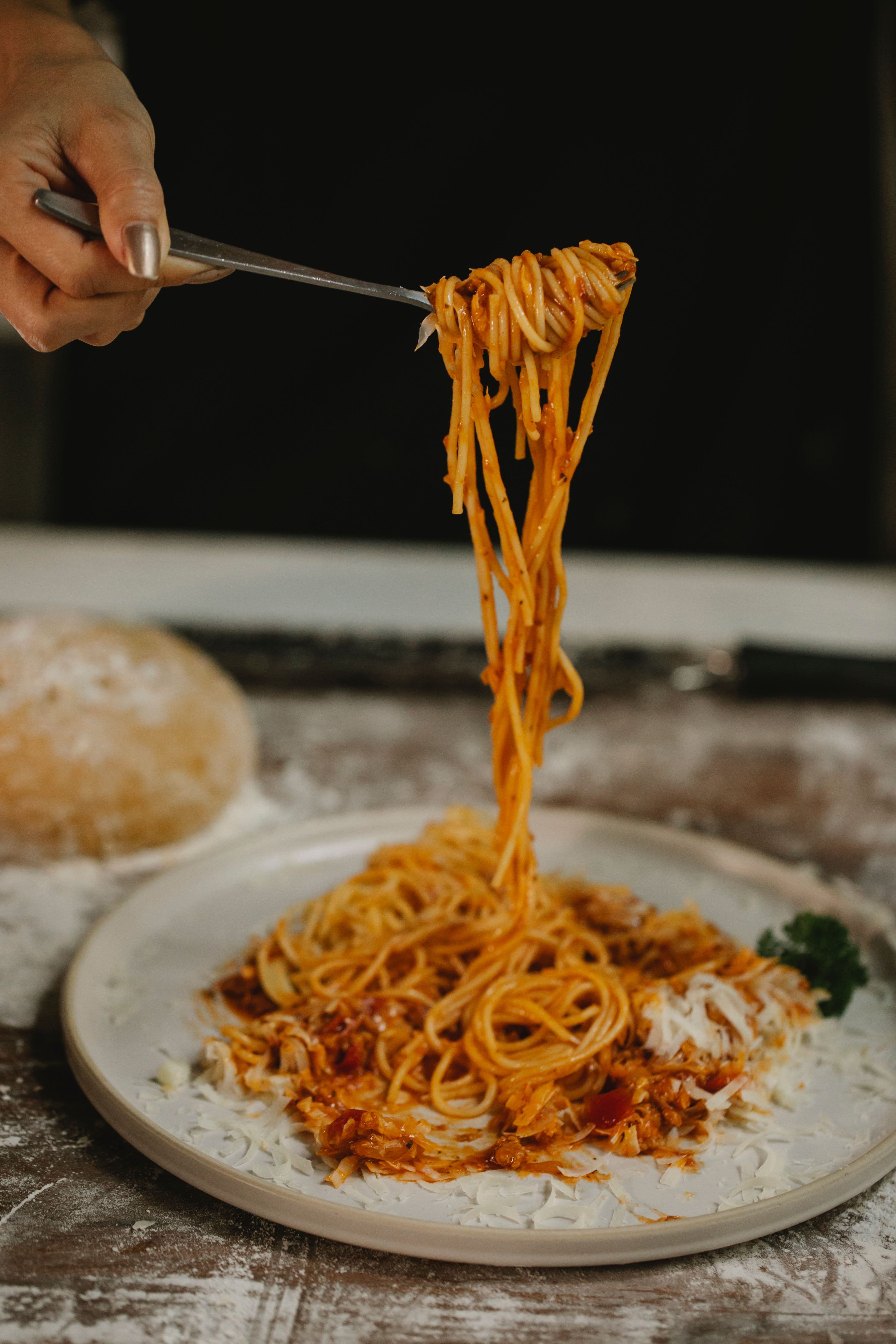 Spaghetti lifted on a fork above a plate dusted with Parmigiano
